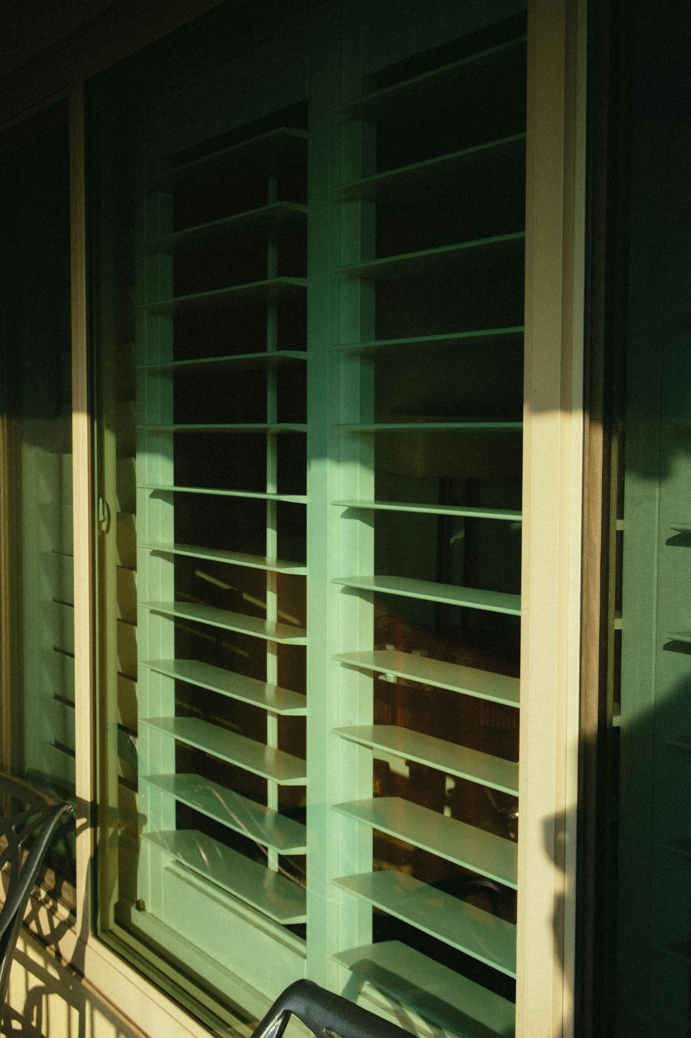 photo by athena sandrini Close-up of a sunlit jalousie window with geometric patterns and green hues.